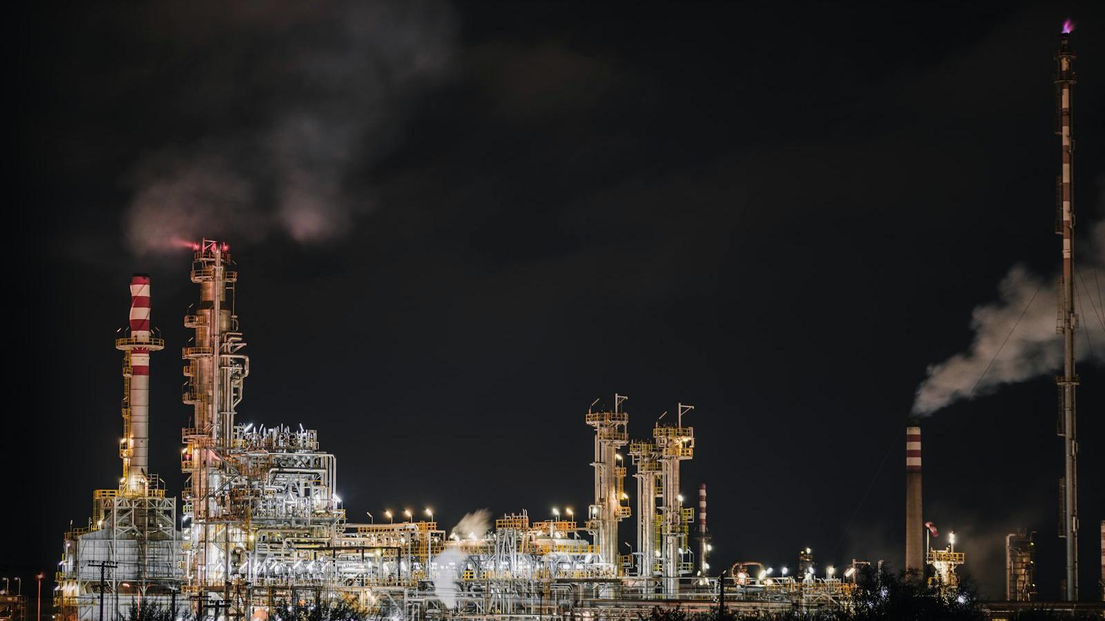 Refinery and process stacks silhouetted against a dark sky at dusk