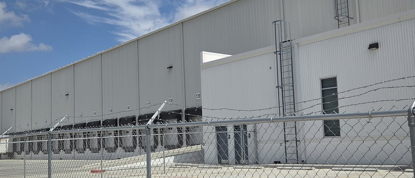 Exterior of the Tetrad Laredo warehouse: a tilt-wall, dock-high facility behind a secured perimeter fence under a bright sky