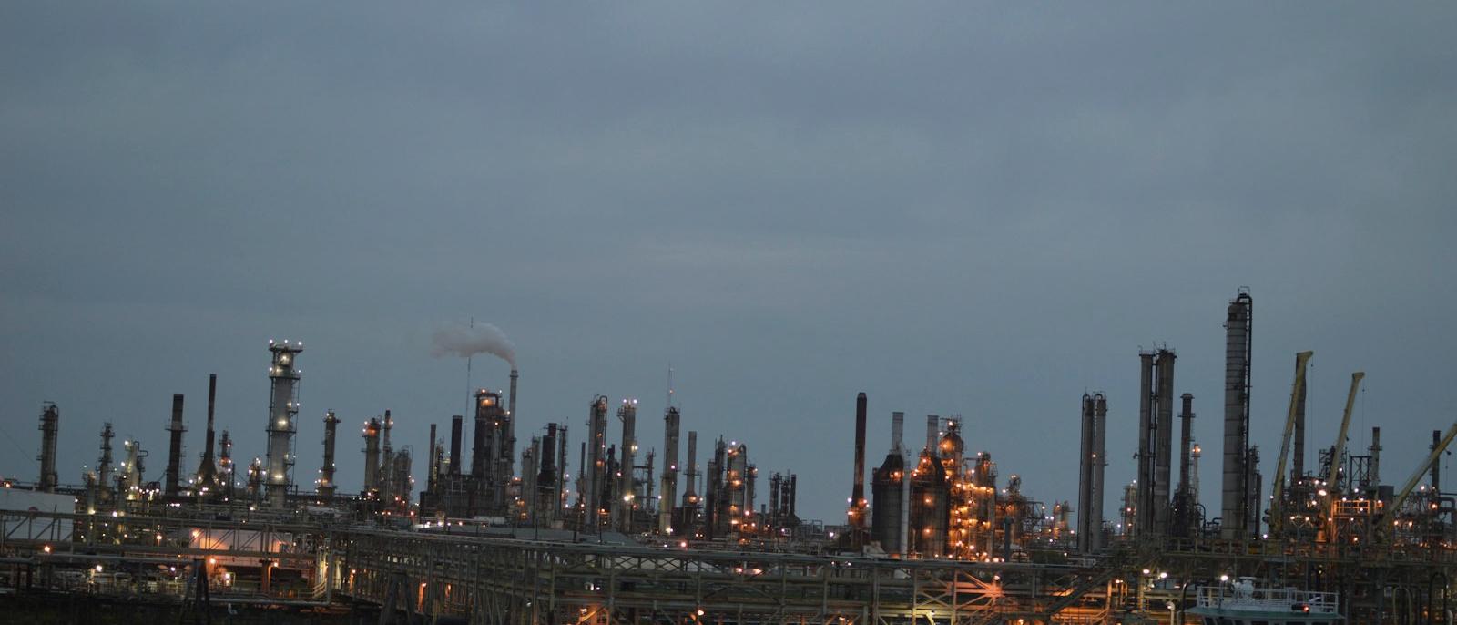 Industrial waterfront at dusk with refinery infrastructure on the horizon